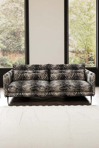 The Lola 4 Seater Sofa in Zebra Print Velvet styled with a rug in front of two windows.