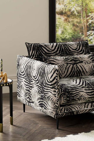 Close-up of one side of The Lola Snuggle Seat in Zebra Print Velvet, styled with a side table and candle holder in front of a window.