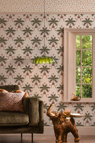 The Midnight Palms Wallpaper in Ivory shown in a living room with a green velvet sofa and an elephant side table. 
