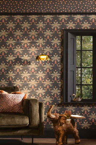 The Midnight Palms Wallpaper in Noir shown in a living room with a green velvet sofa, black paintwork around the windows an elephant side table. 