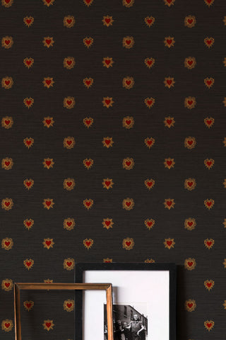 Close up of The Sacred Hearts Wallpaper in Noir Red, against some photo frames. 