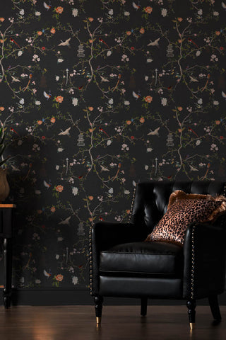 The Secret Garden Chinoiserie Wallpaper in Black Ink shown with a black faux leather armchair. 