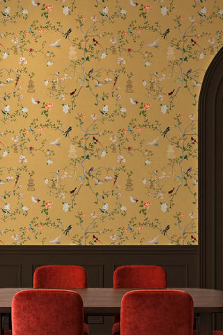 The Secret Garden Chinoiserie Wallpaper in Golden Hour shown in a dining room with rust velvet chairs. 