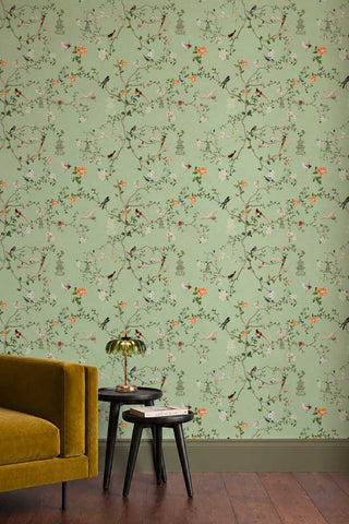 The Secret Garden Chinoiserie Wallpaper in Green Tea shown in a living room with a velvet sofa and side tables. 