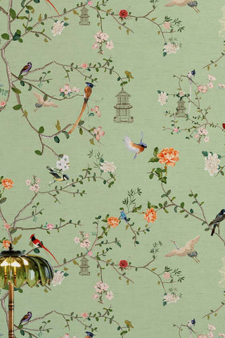 Detail of The Secret Garden Chinoiserie Wallpaper in Green Tea shown with a glass table lamp in the corner. 