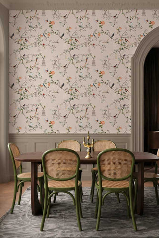 The Secret Garden Chinoiserie Wallpaper in Ivory shown in a dining room with panelled walls, a wood dining table and rattan chairs. 
