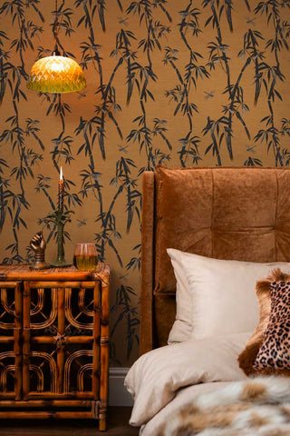 The Wham Bamboo Wallpaper in Golden Hour Noir shown in a bedroom with a bamboo cabinet and velvet headboard. 