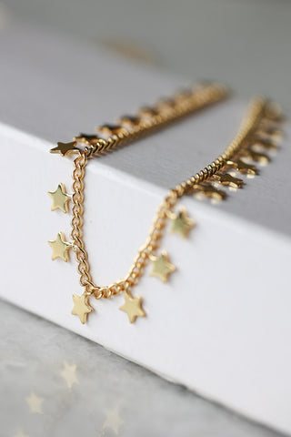 Lifestyle image of the You're A Star Charm Gold Bracelet  draped over a white wooden surface. 