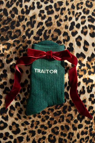 The Traitor Green Glitter Socks displayed against a leopard print background with a red bow across the top. 