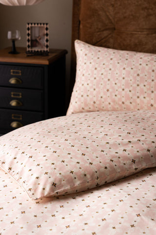 Close-up of the Blush Pink Daisy Bedding Set with Piped Edge styled on a bed, with a bedside table in the background.