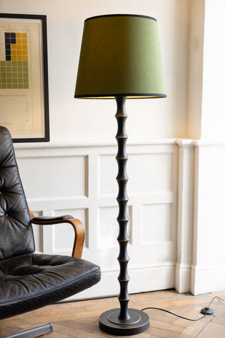 The Vintage-Inspired Floor Lamp With Green Lampshade switched on and displayed next to a swivel chair and art print.
