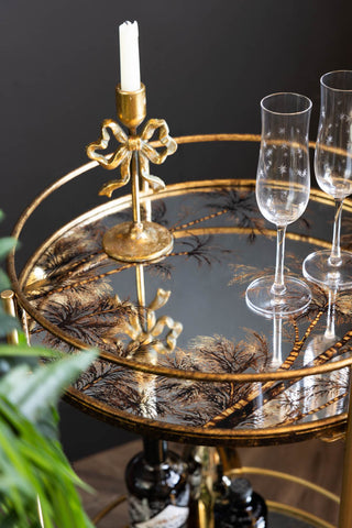 The top shelf of the Vintage Palms Gold Mirrored Drinks Trolley, shown with a gold candleholder and star flute glasses. 