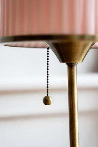 A close-up image showing the gold pull tie on the Vintage Pink Fluted Glass Table Lamp that turns the light on. 