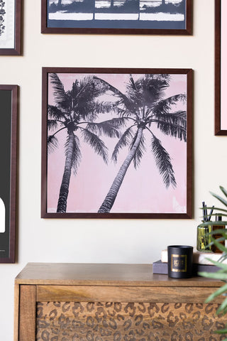 Framed artwork of palm trees on a wall above a wooden cabinet.