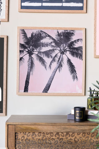 Framed artwork of palm trees on a wall above a wooden cabinet.