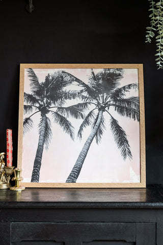 Lifestyle image of Vintage Pink Palms 50cm x 50cm Art Print in a natural frame on a dark background.