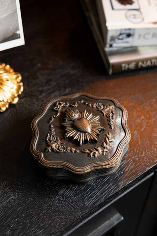 The Vintage-Style Milagro Heart Trinket Box shown on a black console table amongst books and other treasures. 