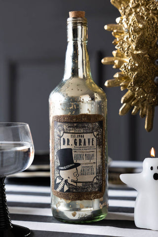 Vintage-style bottle labeled 'Dr. Grave' on a decorative table with a ghost and candle.