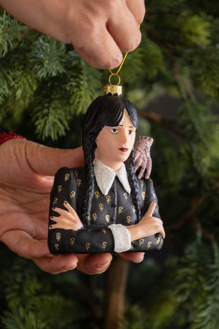 Decorative ornament of a character with dark hair and a mouse, held against a green Christmas tree background.