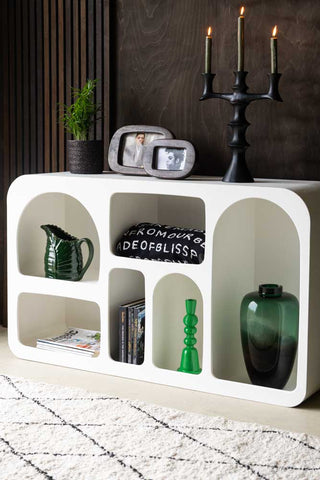 Lifestyle image of the White Alcove Shelf styled with various home accessories inside and on the top, displayed in front of a dark wooden wall and next to a rug.