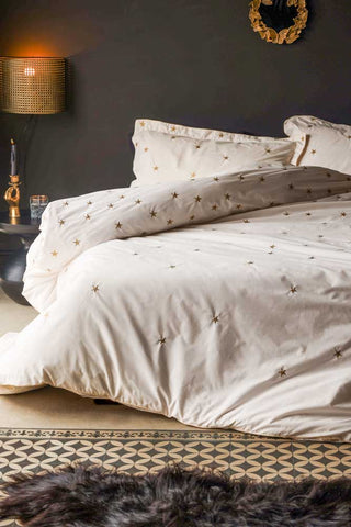 Lifestyle image of the White Falling Star Cotton Bedding Set styled on a bed in front of a black wall with various home accessories.