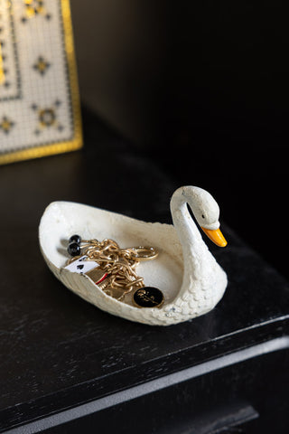 The White Swan Cast Iron Trinket Dish shown holding jewellery on a black wood console. 
