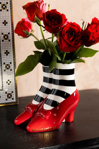 The Wizard of Oz 'Wicked Witch' Shoe Vase shown against a plaster wall with red roses in the vase. 