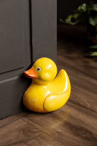 The Yellow Duck Cast Iron Doorstop styled in front of a black door with a plant in the background.