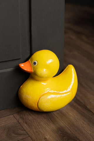The Yellow Duck Cast Iron Doorstop in front of a black door.