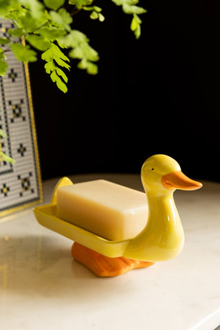 The Yellow Duck Soap Dish styled with some soap on, with a mirror and a plant also in shot.