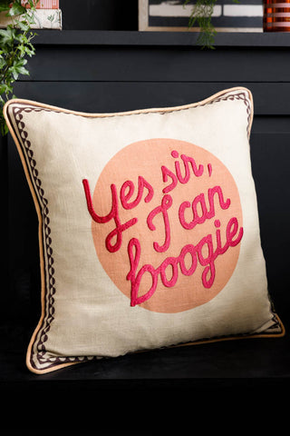 The Yes Sir, I Can Boogie Embroidered Cushion styled on a black bench with plants on the shelf above