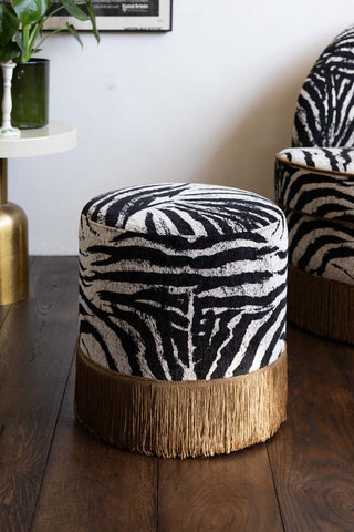 The Zebra Print Tassel Footstool shown against the matching swivel chair in a neutral room. 