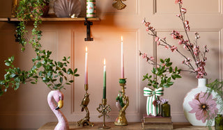 Decorative setup with candles, plants, and a flamingo figurine against a wooden panel wall.