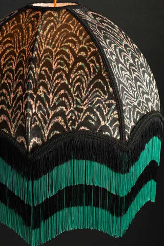 A large pattered lampshade in an Art Deco style with black with a teal and black fringing on the bottom. 