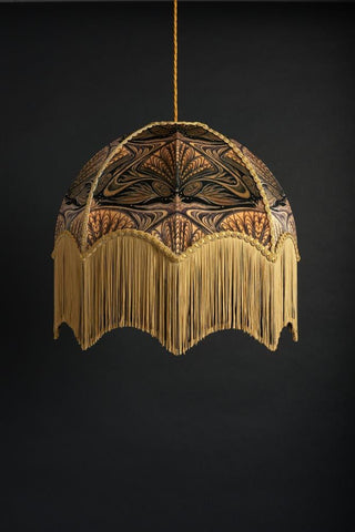Image showing Anna Hayman lampshade in 'oyster' printed design with gold tassels, hung in front of a black wall. 