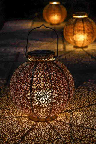 An image of three lit Moroccan style lanterns, casting pretty patterned shadows on the floor. 
