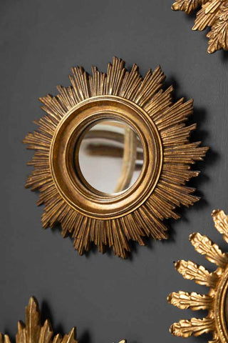 Round decorative sun-shaped gold mirror displayed on a wall, with other decorative gold pieces surrounding the edges. 