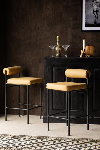 Two Sand Faux Leather Roll Back Bar Stools displayed in front of a black wooden cabinet styled with home accessories on the top.