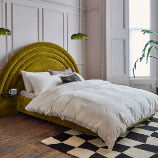 A large bedroom with a very big kind size bed in velvet antique green with built-in bedside tables. Suspended either side of the bed are two green glass shade ceiling lights.