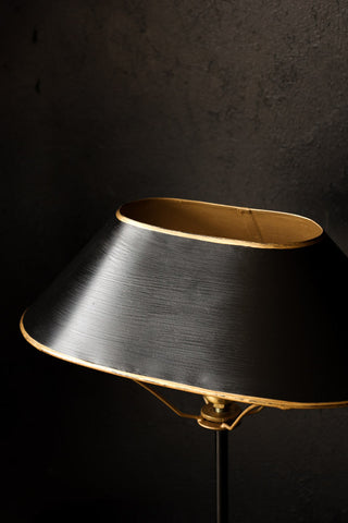 close up image of black & gold table lamp on black table with dark wall background