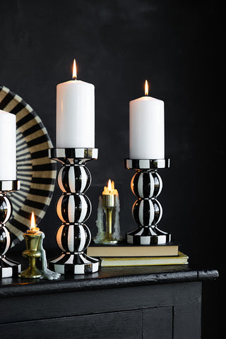 Two black and white striped candle holders of different sizes styled with lit candles inside, on a black sideboard with various other home accessories.