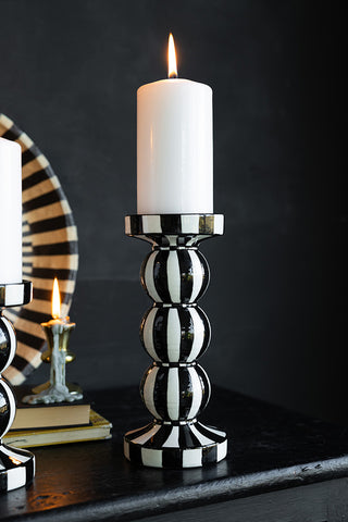 A black and white striped candle holder with a lit candle inside, styld on a black  surface wth some other accessories.