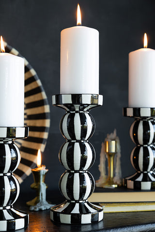Three monochrome striped candle holders styled with lit pillar candles inside, displayed on a sideboard with other lit candles, a bowl and a book.