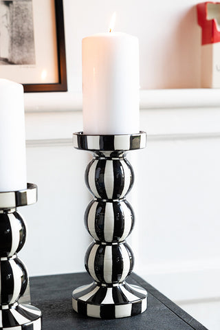 A tall black and white candle holder with a lit candle inside, displayed on a black sideboard with another smaller version.