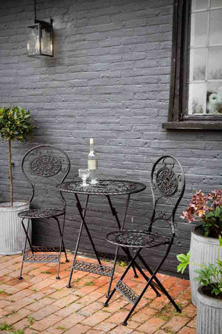 A metal garden set of an oval black metal table with two metal chairs in a decorative metalwork finish. 