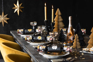 A beautiful christmas table laid with dark floral crackers, mustard christmas trees, glittering glassware and crockery.