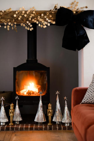 A lit fire place styled with large and small antique trees.