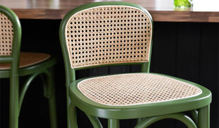 Two green wood and wicker bar stools styled in front of a kitchen island.