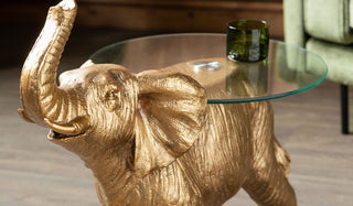 A gold elephant shaped side table, styled with a green glass tumbler on top.