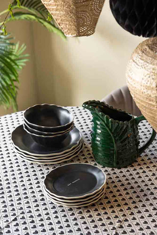 Lifestyle image of the 12 Piece Black Bon Appetit Dinner Set styled with the Green Leaf Water Jug on a heart pattern tablecloth.